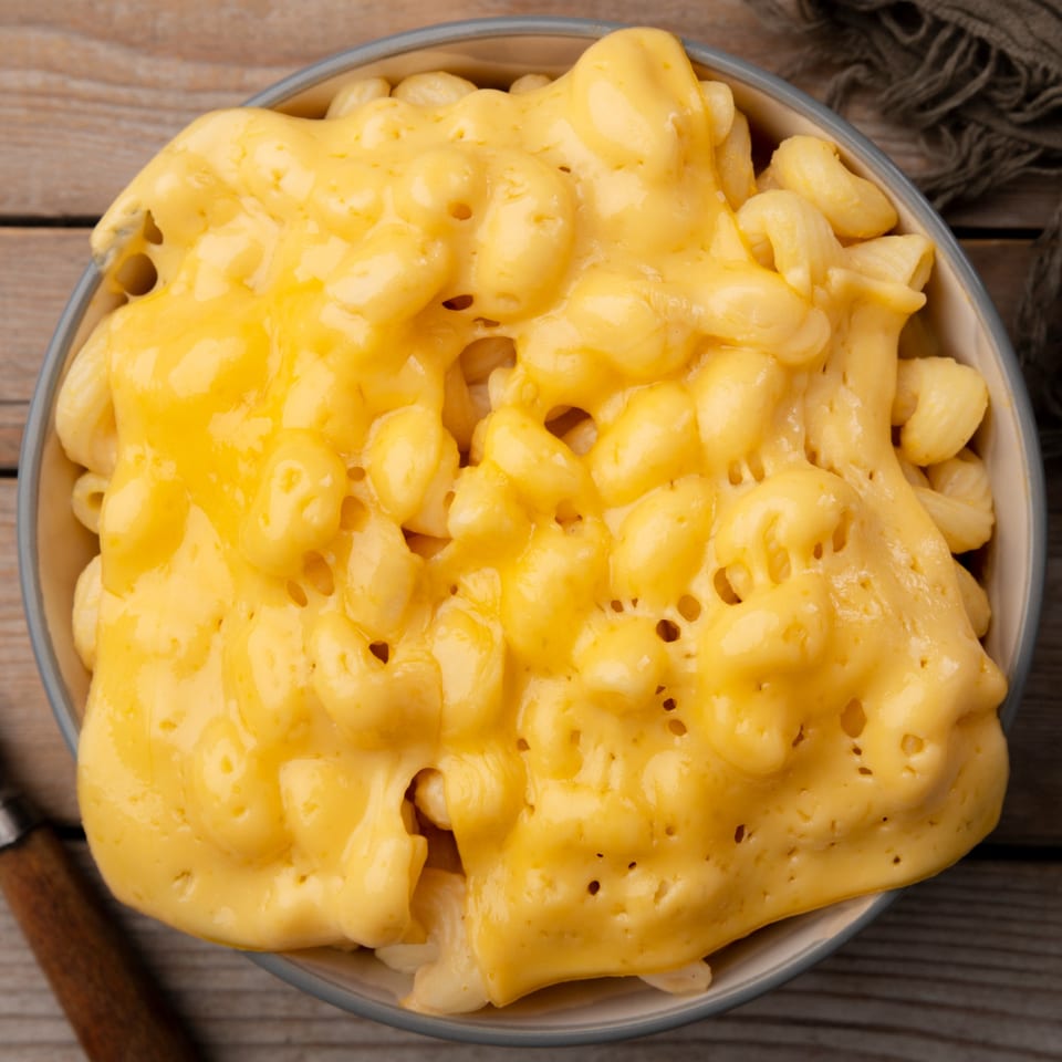 A bowl of Boston Seafood Company's creamy, golden macaroni and cheese on a rustic wooden table.