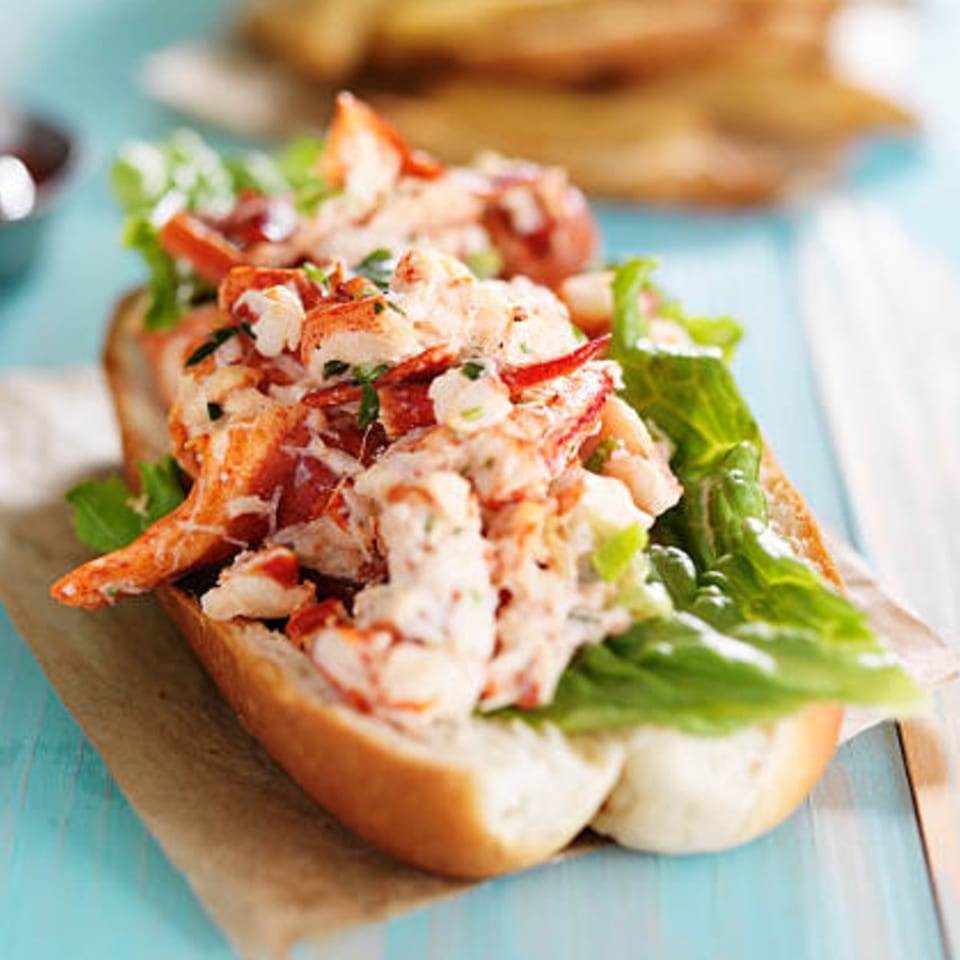 A Boston Seafood Company lobster roll with fresh lobster meat and green lettuce on a bun.
